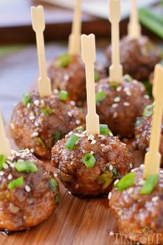 several meatballs with toothpicks in them on a wooden board and garnished with green onions