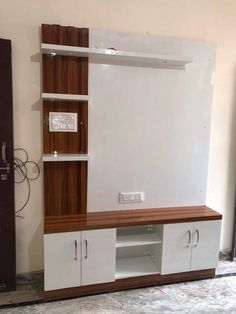 a white entertainment center with wooden shelves and doors on the front, in an empty room