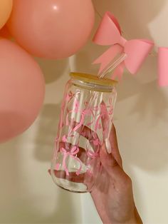 a person holding up a mason jar with pink bows on it and balloons in the background