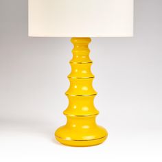 a yellow table lamp with a white shade on the top and bottom part of it