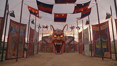 the entrance to an amusement park decorated with flags and banners, including a demon mask