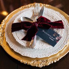 a white plate topped with a red velvet bow and silverware on top of a wooden table