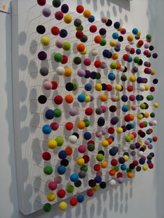 an art piece with many different colored balls hanging from it's sides on a wall