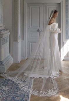 a woman in a white wedding dress standing next to a doorway with a veil on her head