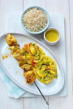 a white plate topped with chicken and veggies covered in sauce next to rice