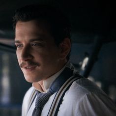 a man wearing a tie and suspenders looking off into the distance in a dark room