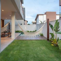 a hammock hanging from the side of a building next to a lawn with a table and chairs