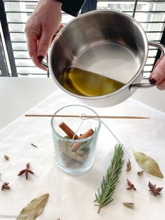 a person pouring olive oil into a glass bowl with cinnamon sticks and anisette