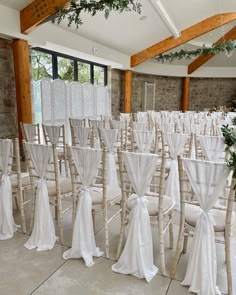 rows of chairs with white sashes and bows on them in an indoor ceremony room