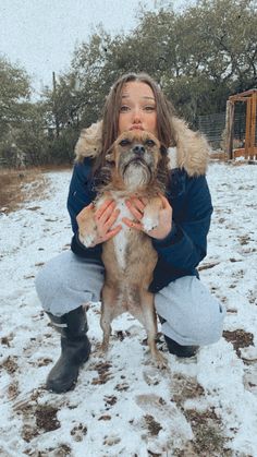 a woman kneeling down holding a dog in the snow