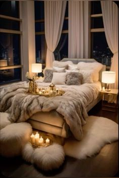 a bed with lots of pillows and blankets on it in front of a window filled with candles