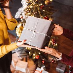 two women holding a gift box in front of a christmas tree