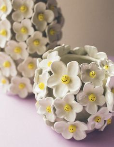 two white and yellow flower vases with smiley faces on them sitting on a purple surface