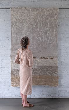 a woman standing in front of a wall hanging on the side of a brick wall