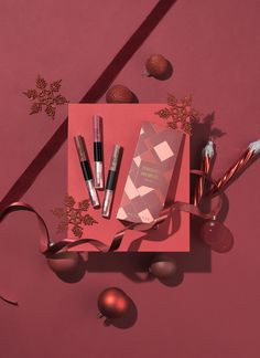 an assortment of cosmetics and christmas decorations on a pink background with red wrapping around it