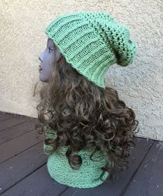 a woman's head wearing a green knitted hat with long curly hair sitting on top of a wooden floor