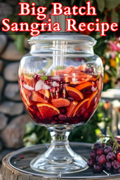 a big batch sangria recipe in a large glass jar on a table with grapes and oranges