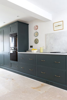 a kitchen with blue cabinets and marble counter tops, gold handles and brass pulls on the doors