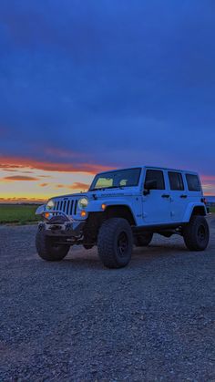 a white jeep parked on top of a gravel road next to the ocean at sunset