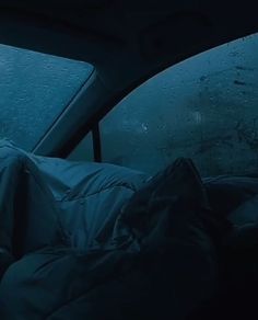 a person sleeping in the back seat of a car on a rainy day with rain coming down