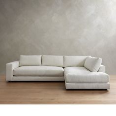 a large white sectional couch sitting on top of a wooden floor next to a wall