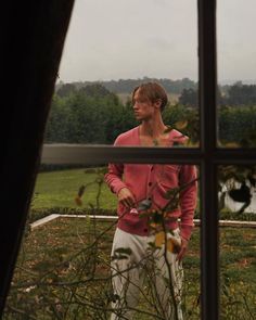 a man standing in front of a window looking out at the grass and trees outside