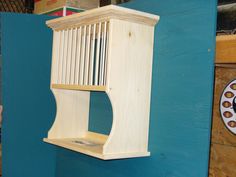 a wooden bird feeder hanging from the side of a blue wall