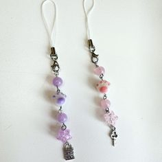 two pairs of earrings with charms attached to them on a white surface, one is pink and the other is purple