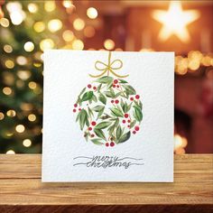 a christmas ornament with holly leaves and red berries is on a card that reads merry christmas