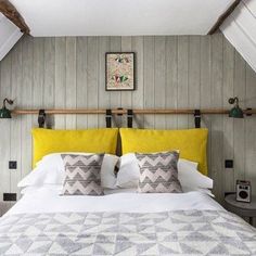 a bed with yellow and gray pillows in a room that has wood paneling on the walls