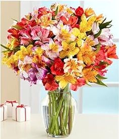 a vase filled with lots of colorful flowers on top of a table next to a gift box