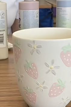 a cup with strawberries painted on it sitting on a table next to other items