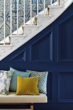 a white staircase with blue walls and colorful pillows on the bench in front of it