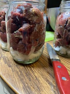 two jars filled with food sitting on top of a wooden table next to a knife