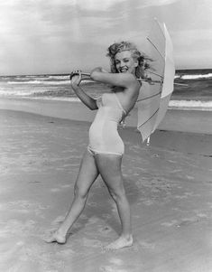 a woman in a bathing suit holding an umbrella on the beach