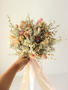 a bouquet of flowers is being held up by someone's hand with the ribbon tied around it