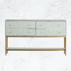 a white and gold dresser sitting on top of a marble counter next to a wall