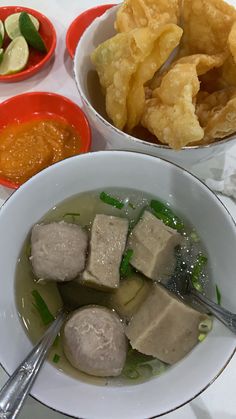 two bowls filled with food next to some dipping sauces and other foods on the table