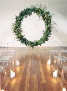 an arrangement of clear chairs with candles and greenery in the middle, along with a wreath on the wall