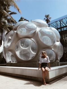 a woman is sitting on a bench in front of a large ball shaped building with many windows