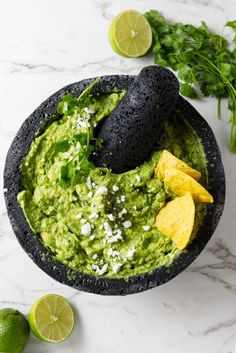 guacamole in a black bowl surrounded by limes and cilantro