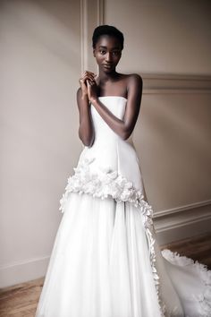 a woman in a white wedding dress with flowers on the skirt and her arms crossed