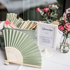 a table topped with flowers and cards next to a vase filled with pink roses on top of a white table cloth