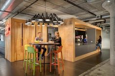 two people are sitting at a table in an office with wood paneling and neon colored chairs