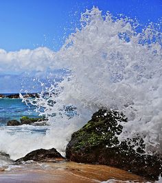 an ocean wave crashes on the rocks at the beach