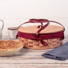 a pie sitting next to a basket on top of a wooden table with a tea pot