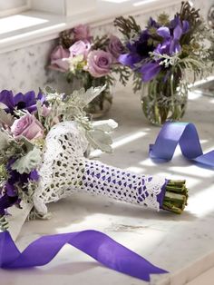 purple and white flowers are in vases on the counter next to blue satin ribbons