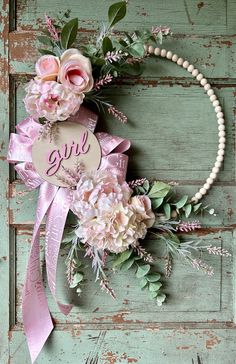 a wreath with pink flowers and greenery hanging on a green wooden door that says girl