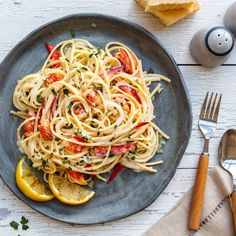 a plate of pasta with tomatoes, lemons and parmesan cheese on the side