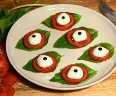 small appetizers are arranged on a plate with tomato slices and leaves around them